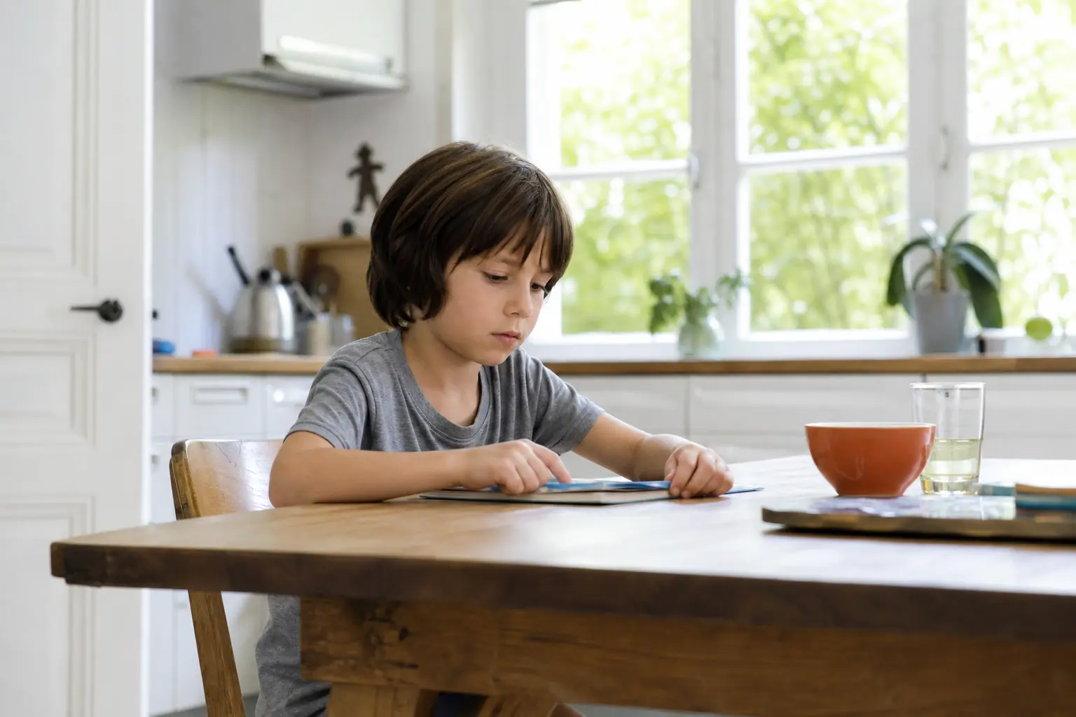 Enfant assis seul à une table de cuisine lumineuse, un verre de lait devant lui, regardant vers la fenêtre