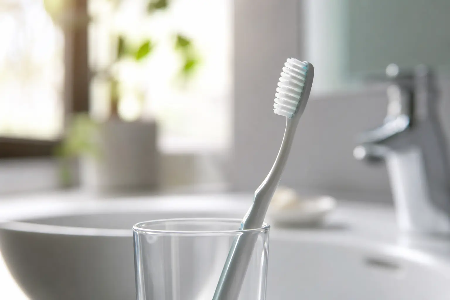 Brosse à dents propre posée dans un verre au bord d'un lavabo de salle de bain lumineuse