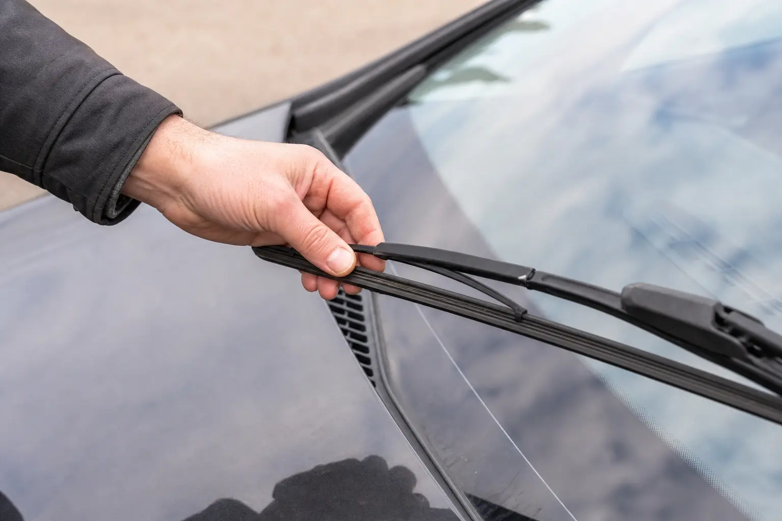 Gros plan sur une main qui vérifie l'état d'un essuie-glace sur le pare-brise d'une voiture, en pleine lumière du jour