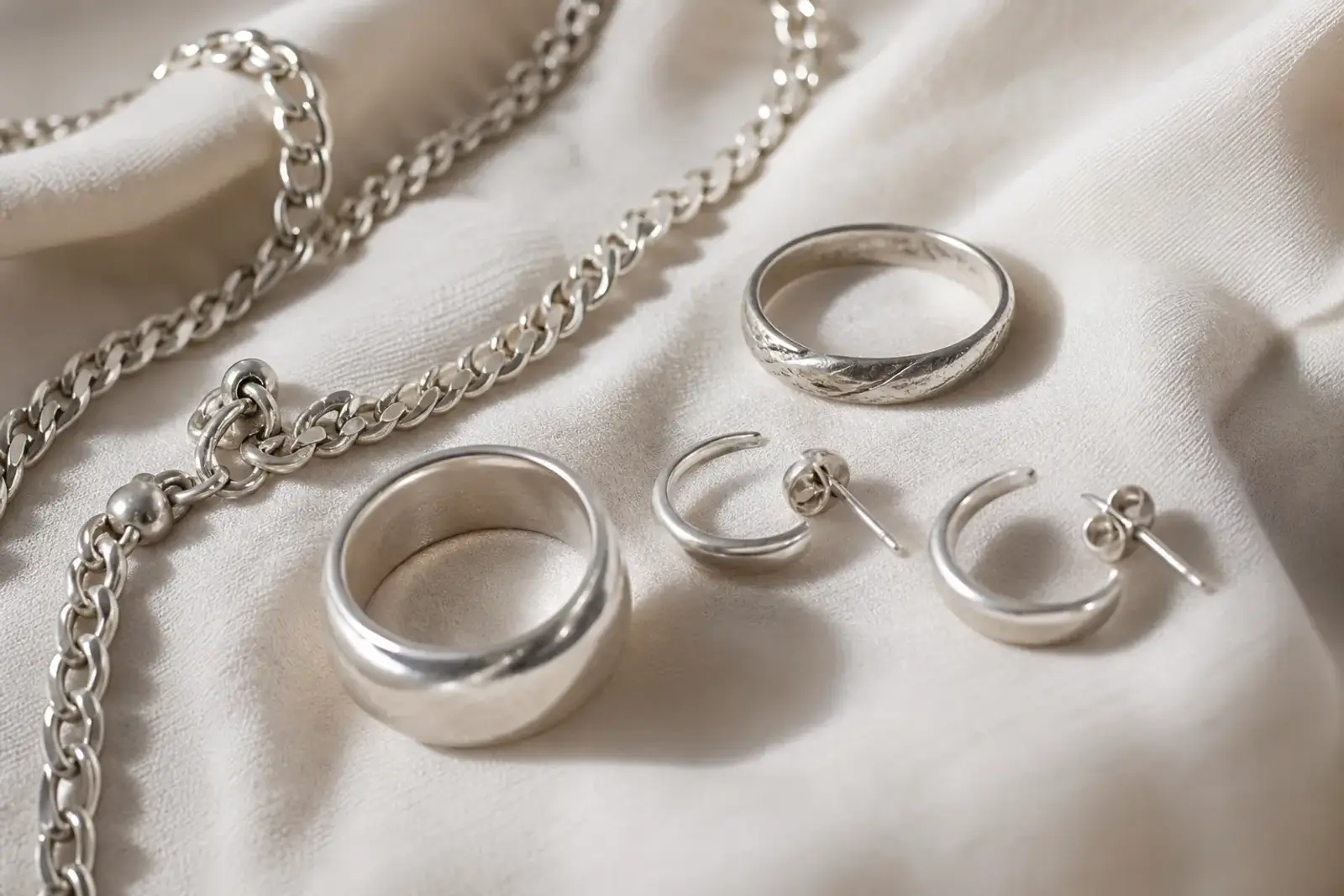 Bijoux en argent, bague et chaîne, posés sur un tissu doux en gros plan, avec un léger contraste entre éclat et ternissement