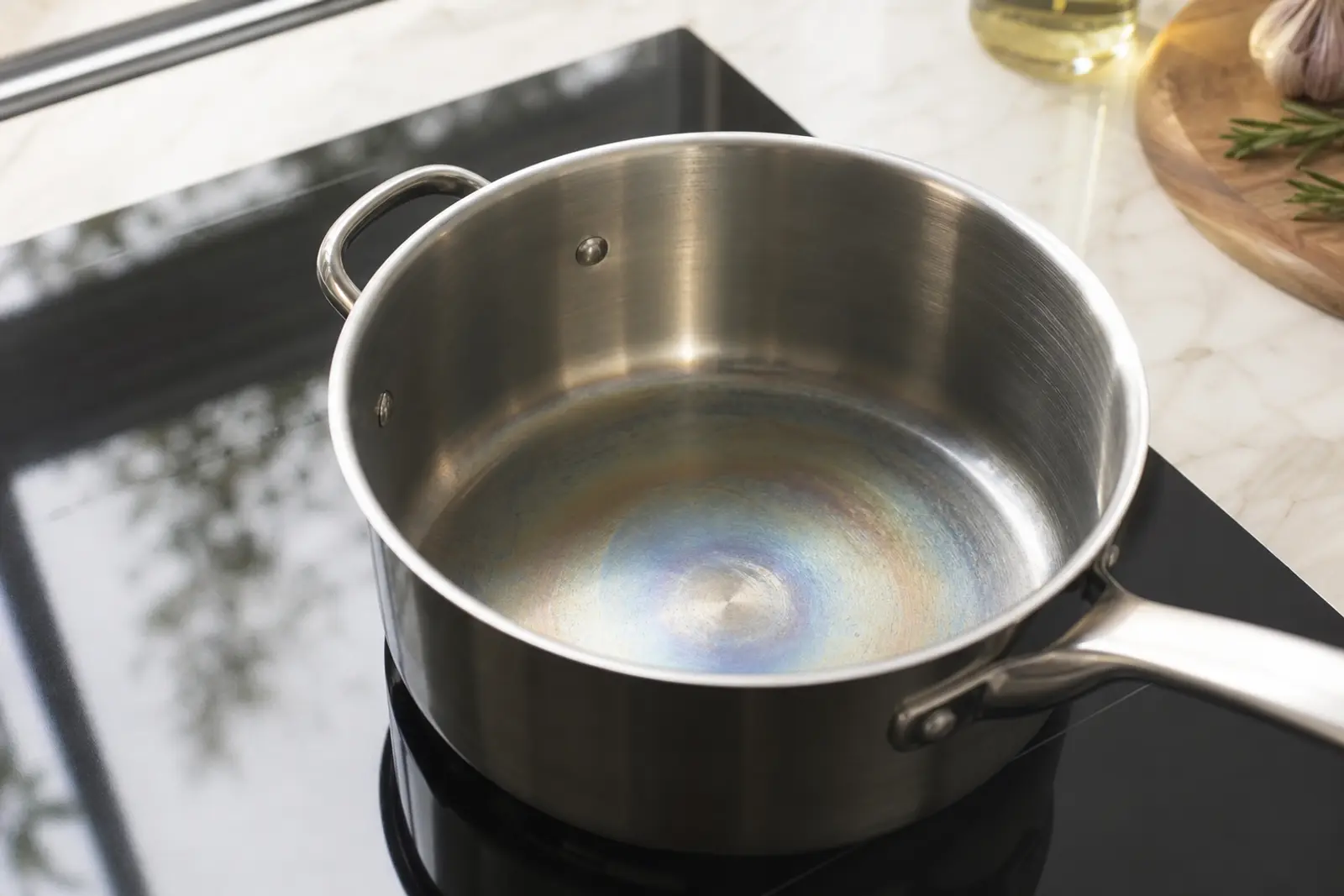 Casserole en inox posée sur une plaque de cuisson, avec des reflets de teinte irisée bleu-doré visibles sur le fond métallique