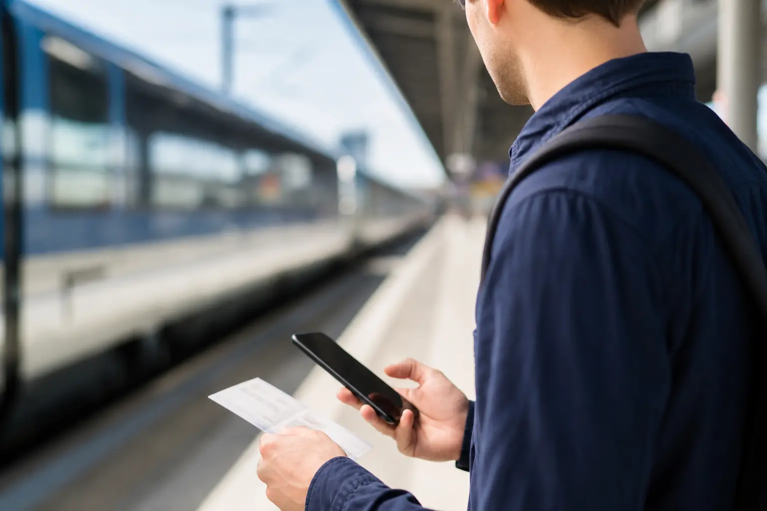 Voyageur consultant un billet de train sur son smartphone sur un quai de gare