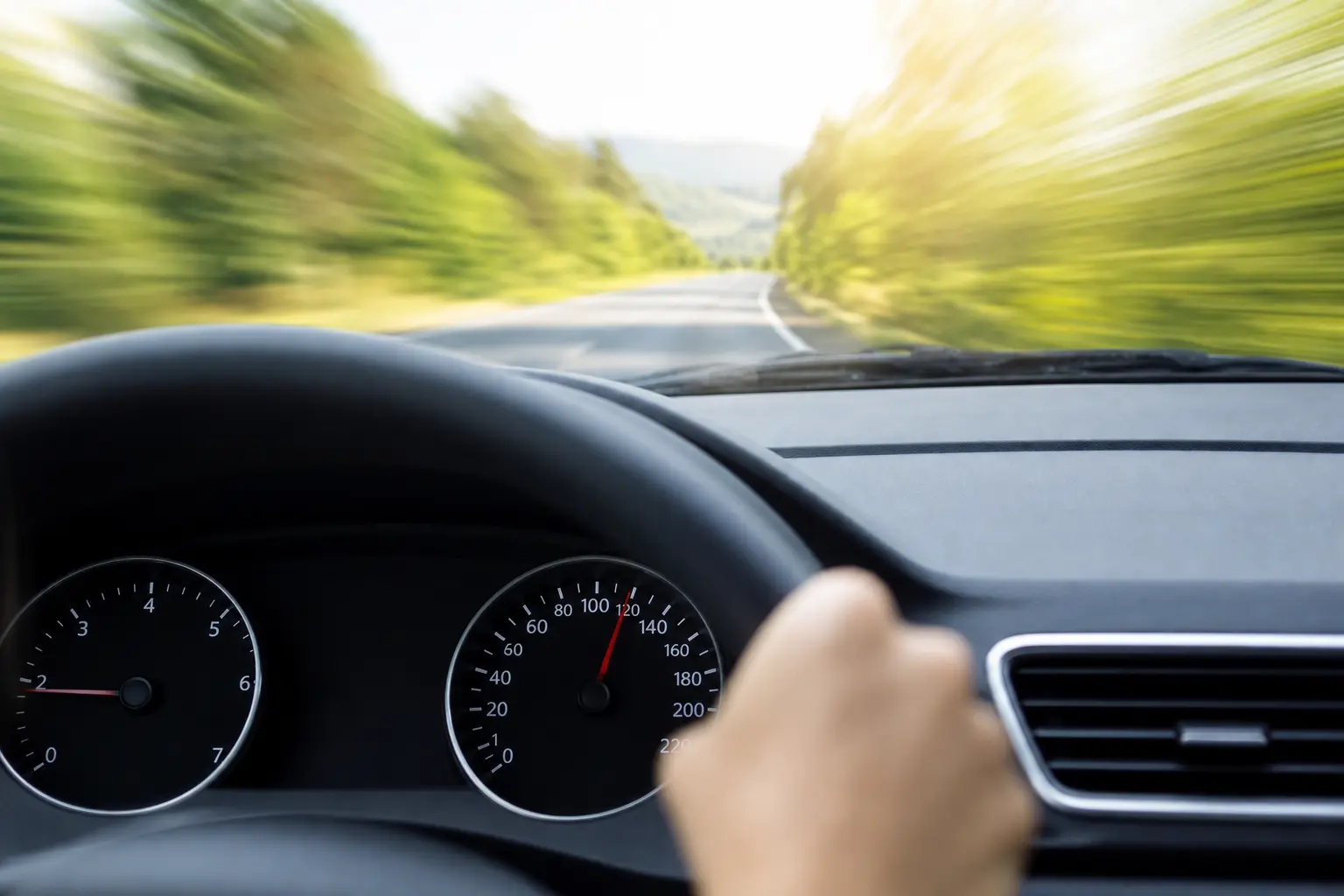 Vue depuis le siège conducteur d'une voiture roulant sur une route de campagne, compteur de vitesse analogique visible sur le tableau de bord, lumière naturelle de journée