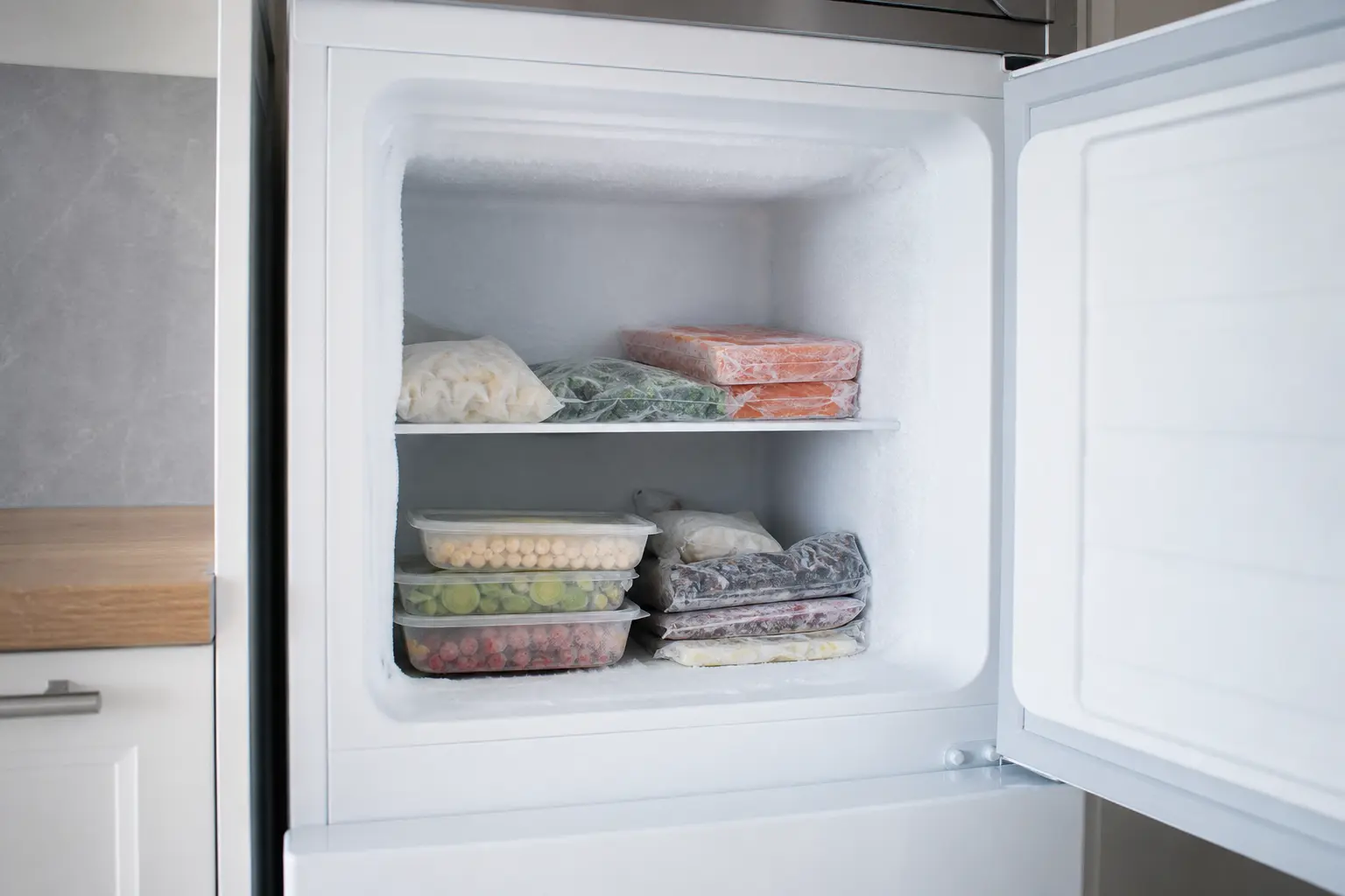 Porte d'un congélateur ouverte révélant une fine couche de givre blanc sur les parois intérieures