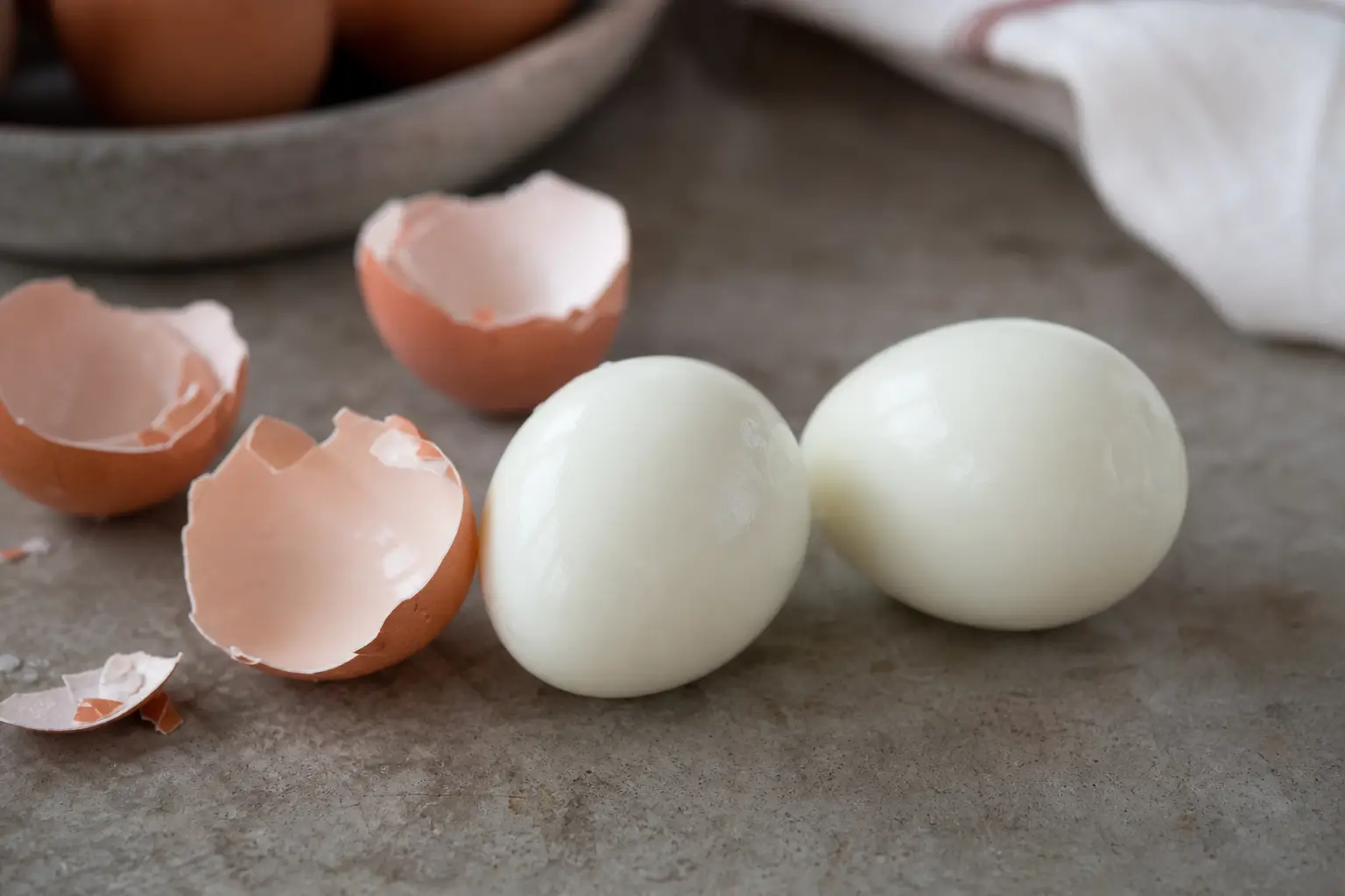 Œufs durs fraîchement écalés posés sur un plan de travail, entourés de morceaux de coquille brisée, lumière naturelle de cuisine