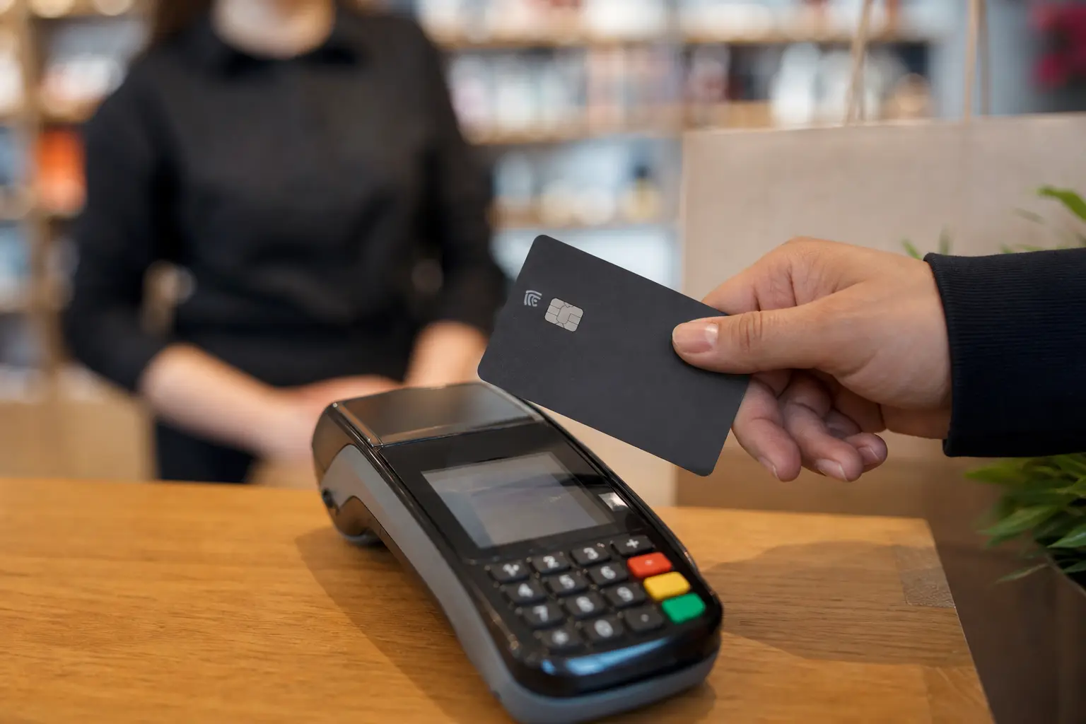 Main présentant une carte bancaire sans contact au-dessus d'un terminal de paiement dans une boutique, lumière naturelle